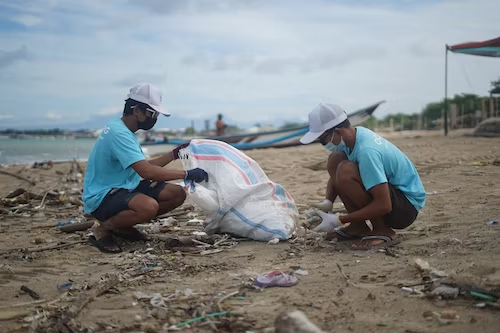 Productive things to do in Jamaica: Beach Clean up.
Man and boy on beach with a bag picking up garbage.