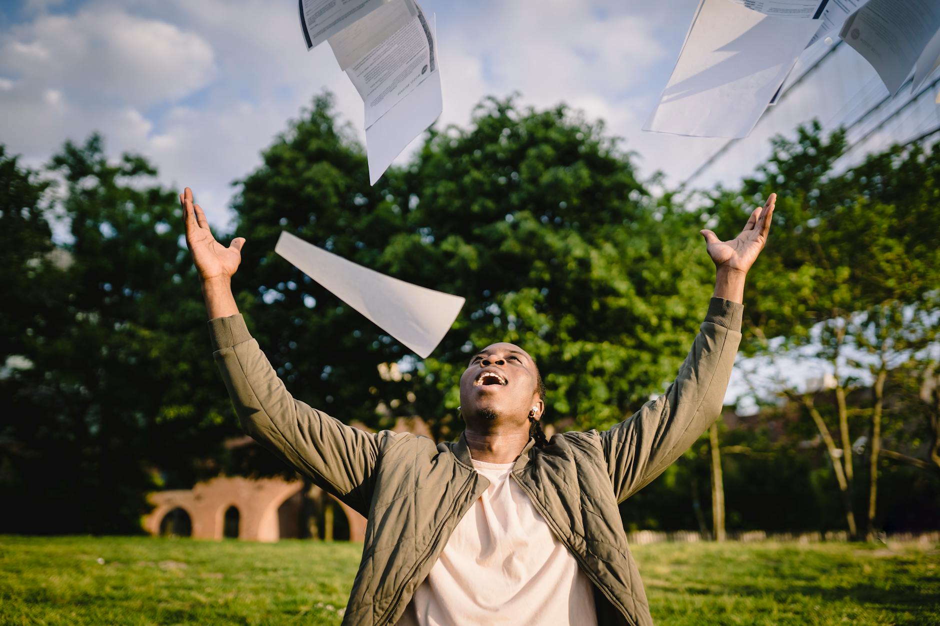 happy student throwing papers in air in park