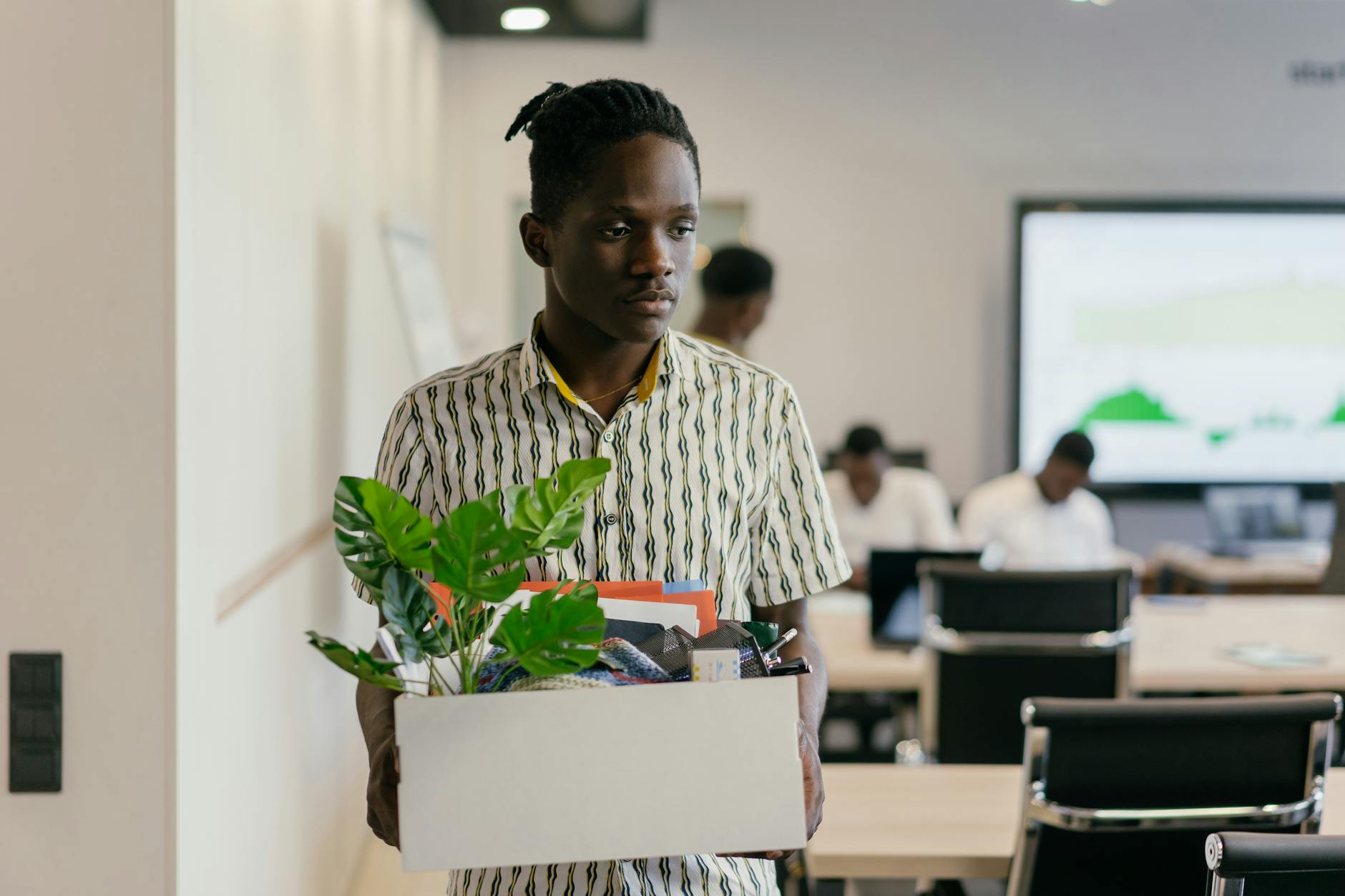 sad man in button down polo carrying white box with green plant and things in it