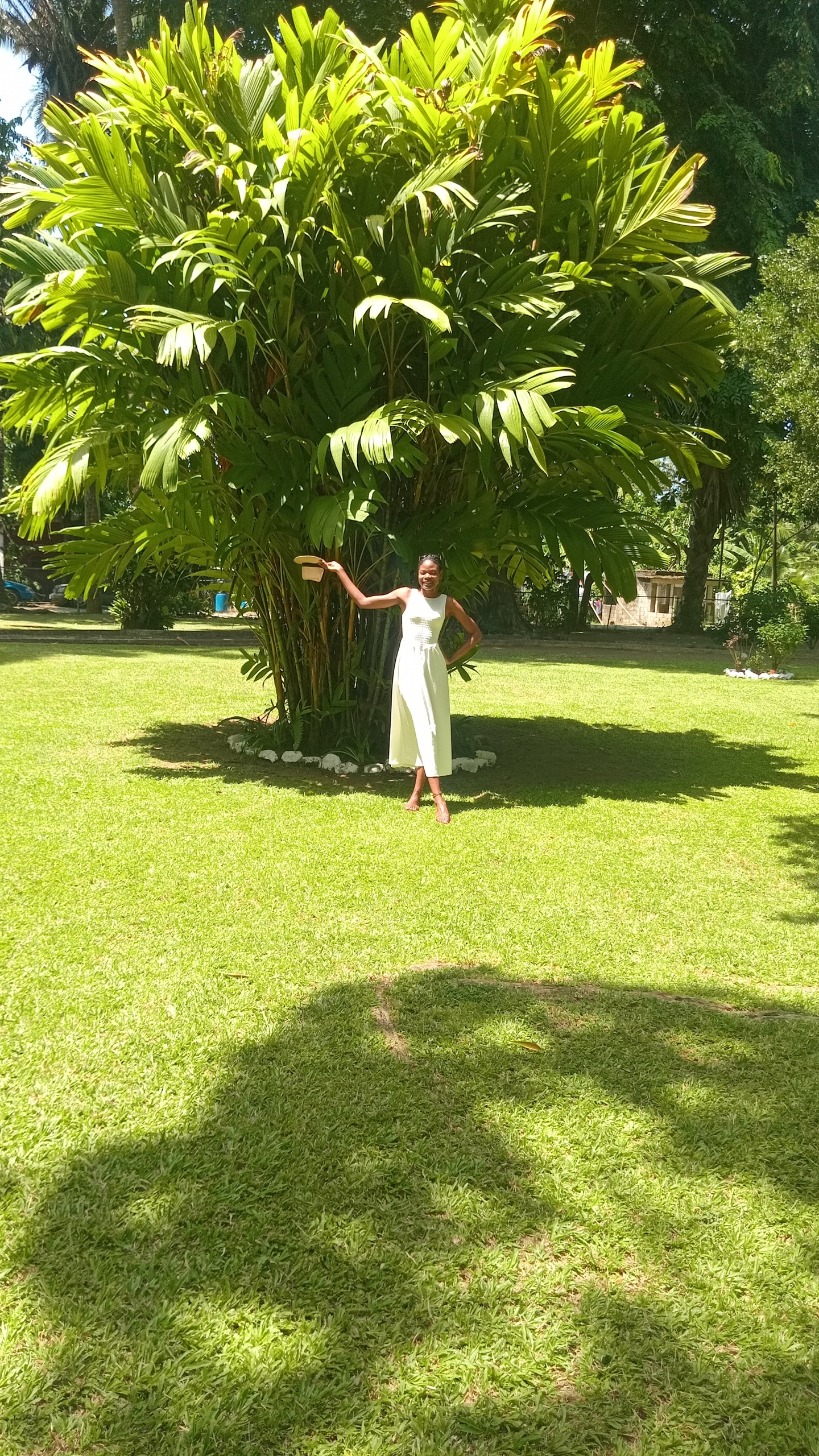 Posing on the lawns of Bath Botanical Gardens in St. Thomas is a lady in a white maxi dress.