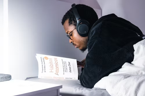 Man laying on bed reading the book Atomic Habits by James Clear.